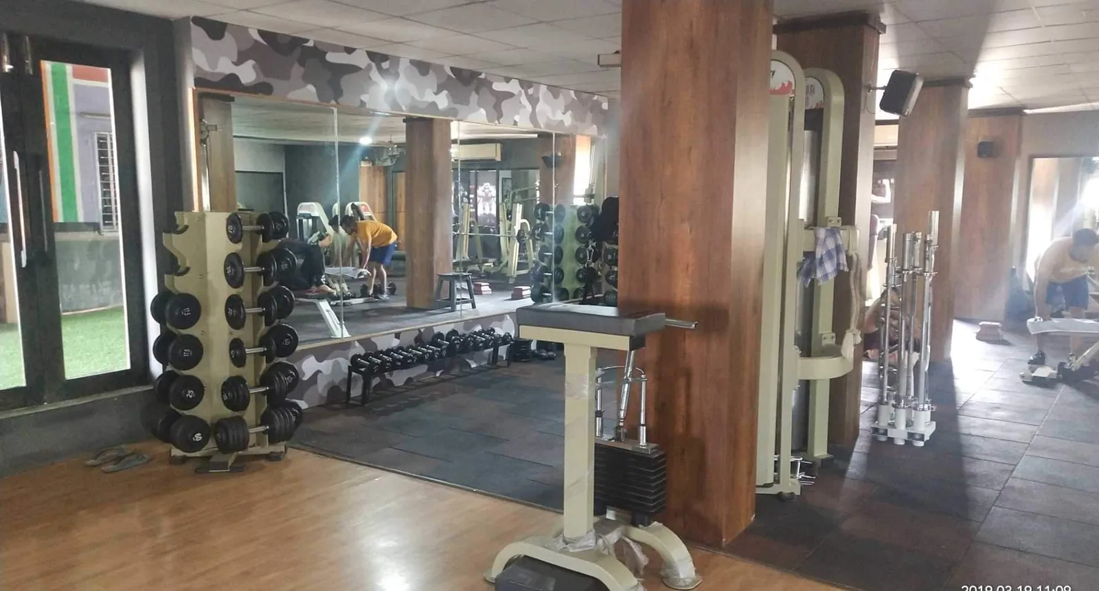 The free weights area at S R Gym Katargam, with a dumbbell tree, mirrored wall and barbell rack