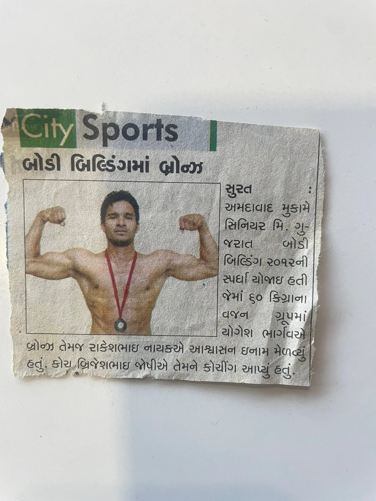 Gujarati newspaper cutting from City Sports reporting a bronze medal in bodybuilding and naming Brijeshbhai Joshi as coach